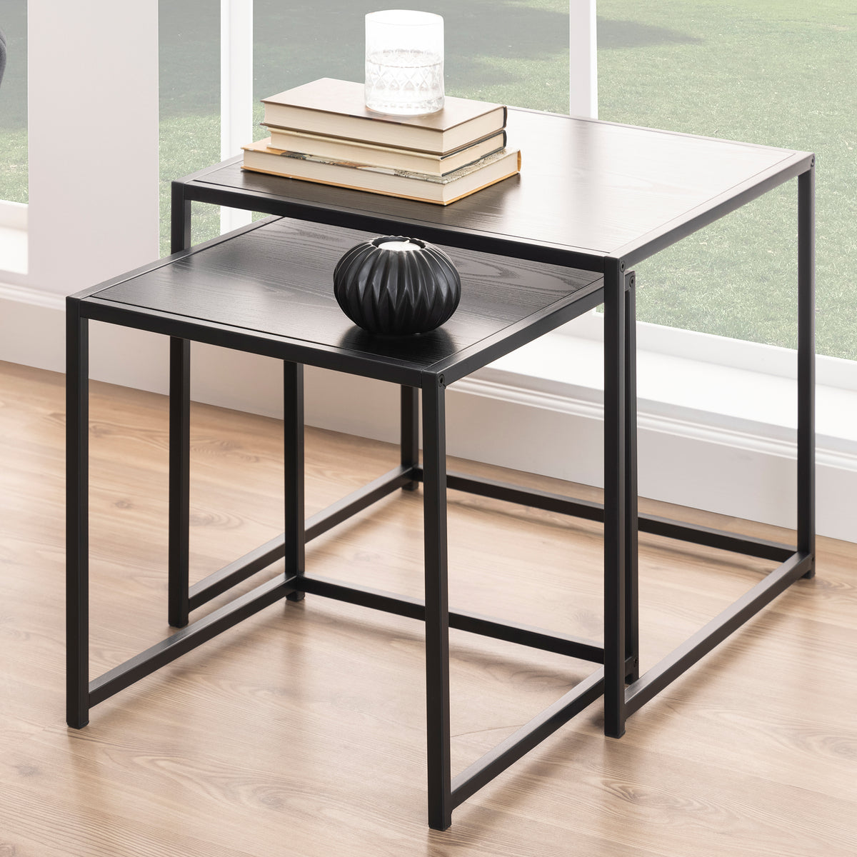 Skeleto 50x45 Black Melamine coffee tables by a large window, with books and a vase – a set of coffee tables for the living room