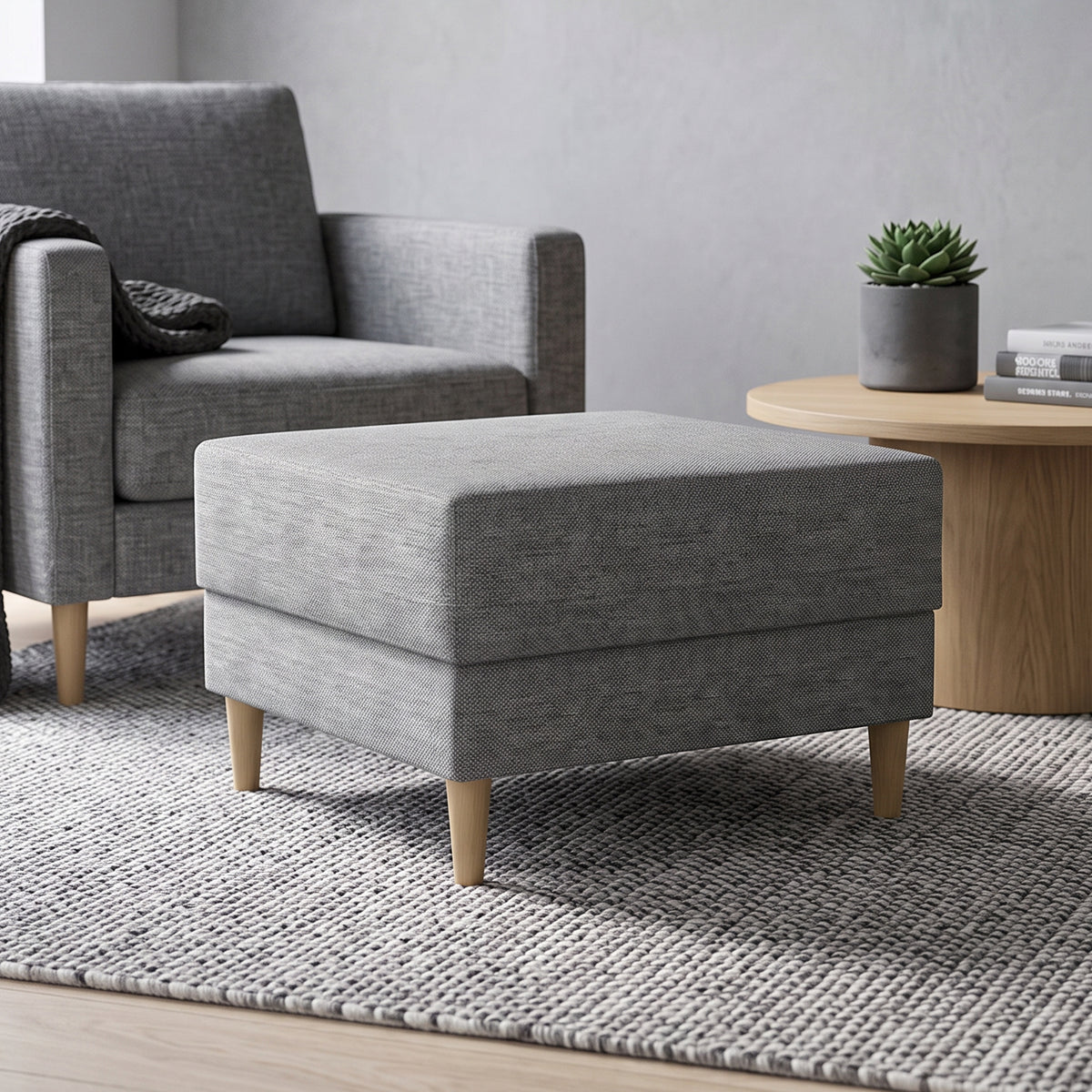 Harmi 66x66 pouffe in the living room in front of a grey armchair, next to a round table with a succulent – pouffe for the living room