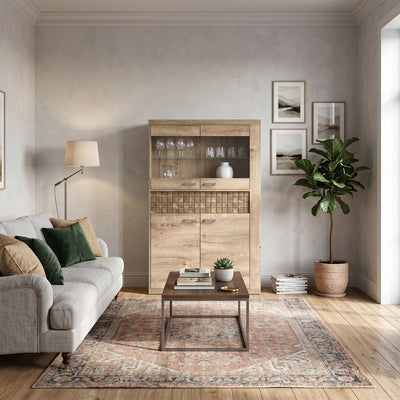 Witryna Korin 102x160 w salonie z szarą sofą i dywanem w orientalne wzory – witryna do salonu z kieliszkami